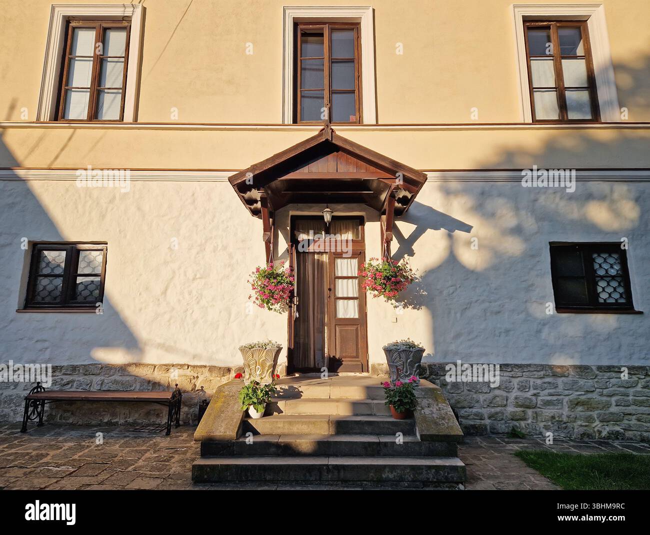 Rustic old building facade with porch and a charming wooden door, framed by two side windows and a small overhang. Stone steps lead up to the entrance - Smartphone Captured Stock Image