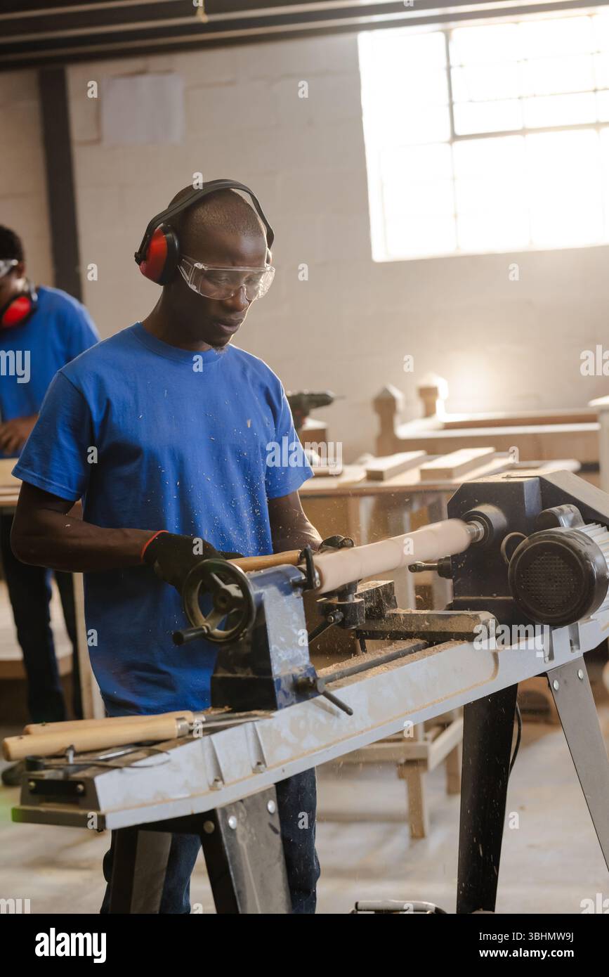 African American man operating wood lathe and shaping wood spindle amid ...