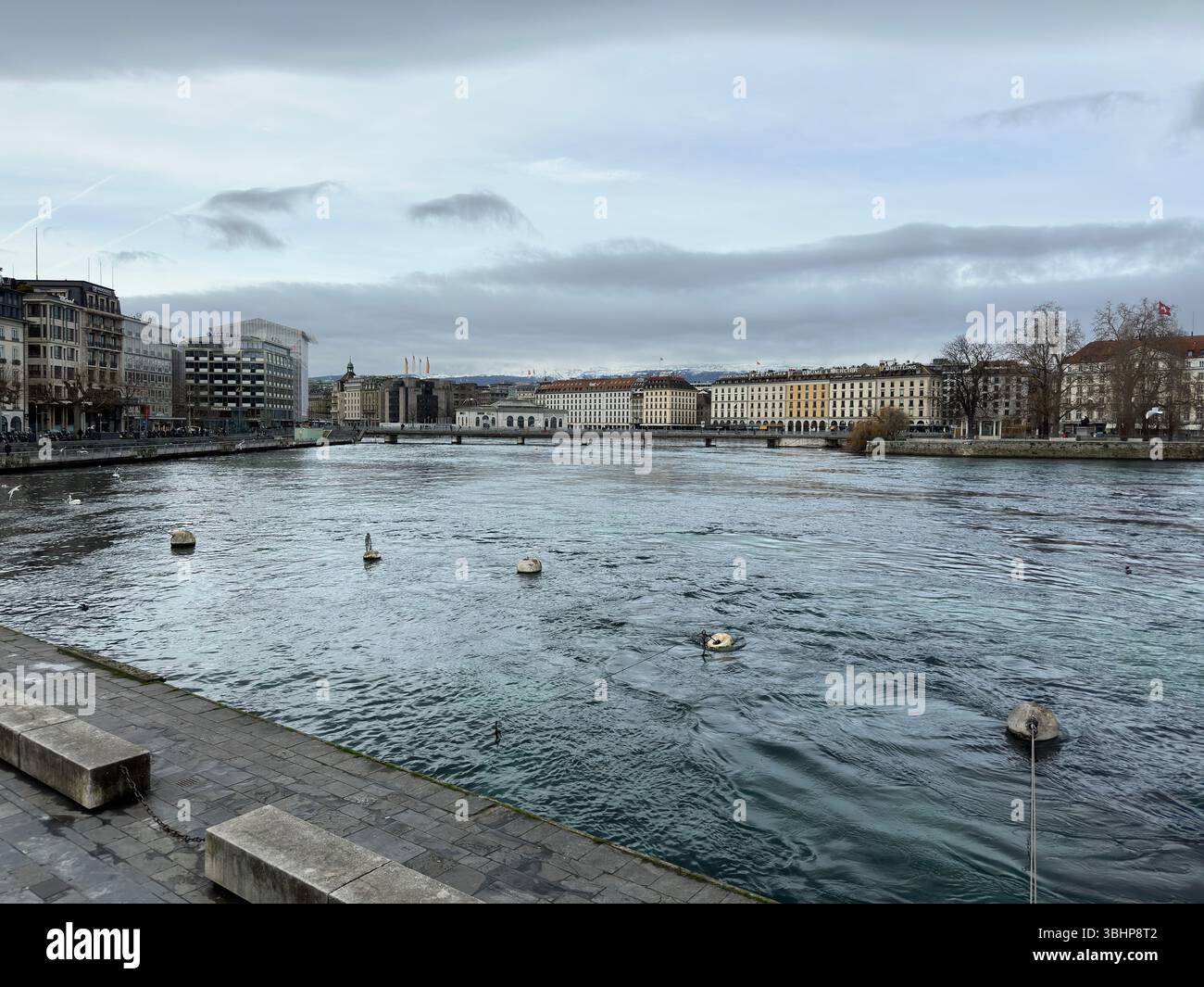 The Rhône River flows through the heart of Geneva on a cloudy day. - Smartphone Captured Stock Image