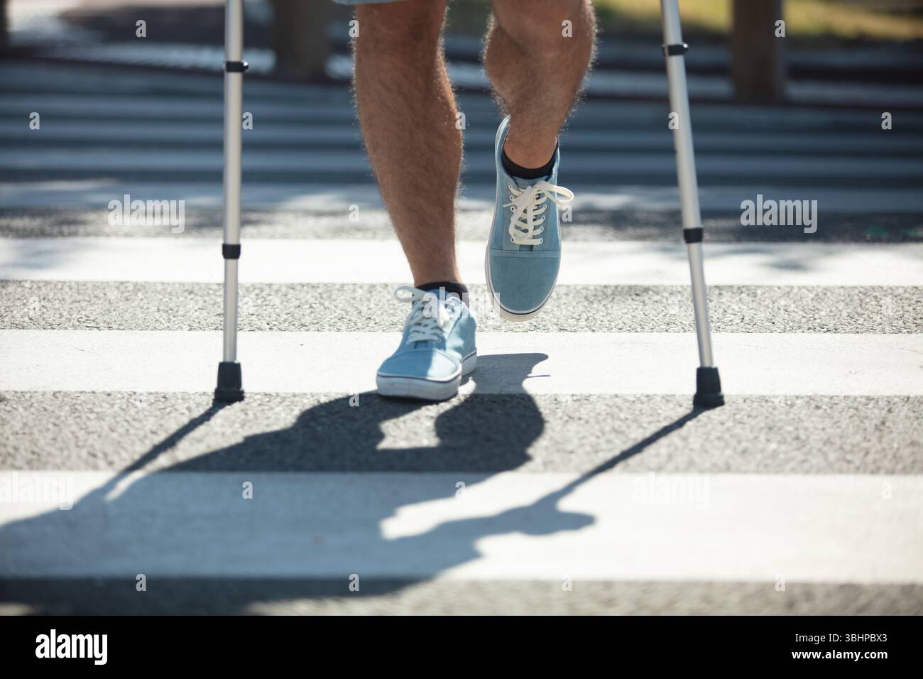 man with crutchen crossing street Stock Photo