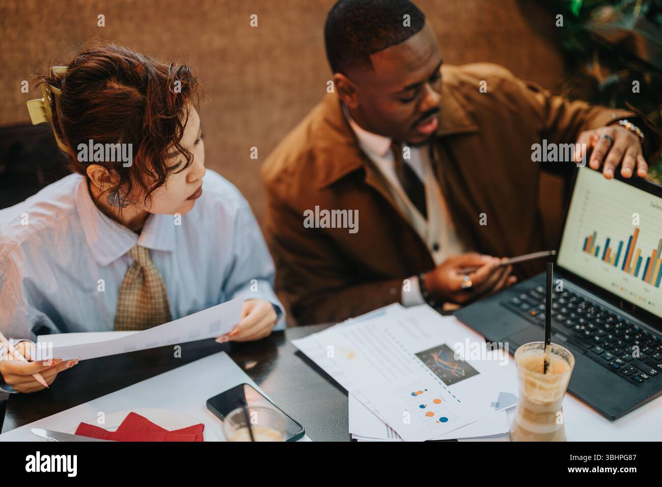 Collaborative business strategy session between two diverse people analyzing data and discussing plans Stock Photo