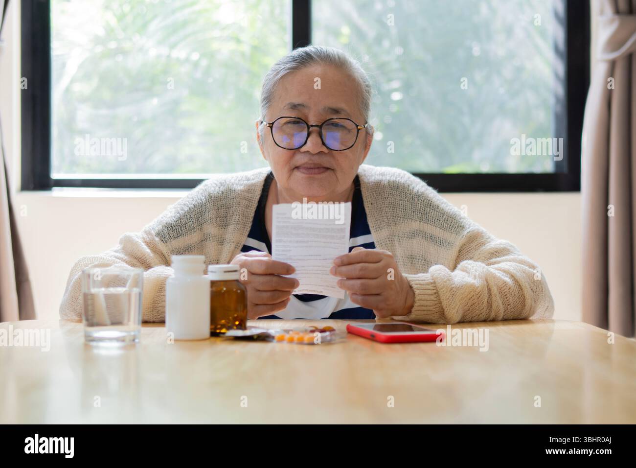 Senior Asian woman sit and reading side effects list of drug and contraindications, checking prescription and dosage of medicine. Retirement heathy co Stock Photo