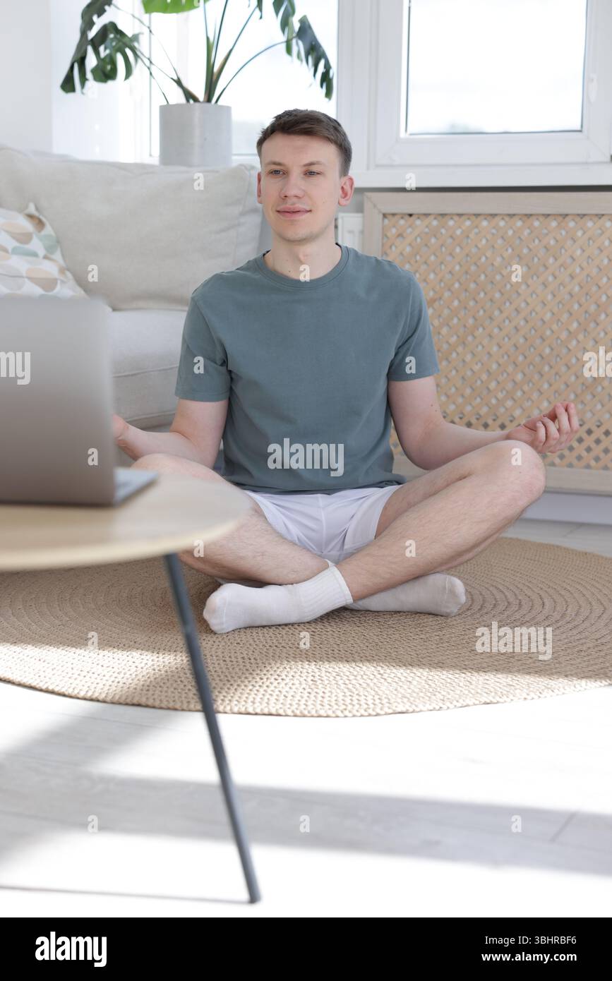 Man having online yoga class via laptop at home Stock Photo