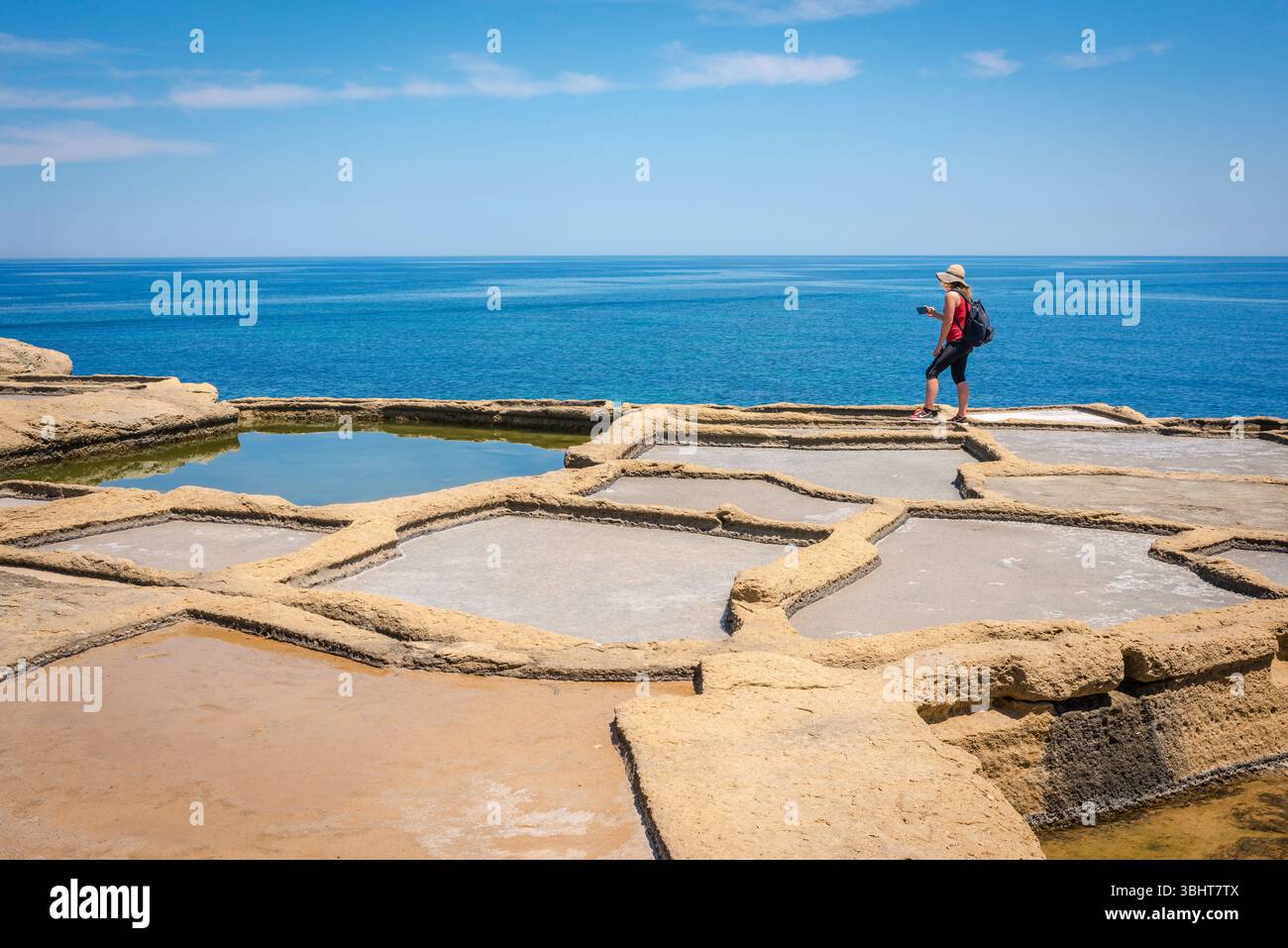 Woman tourist, view of a young female solo traveller wearing a backpack and photographing the scene before her, Gozo, Malta. Stock Photo