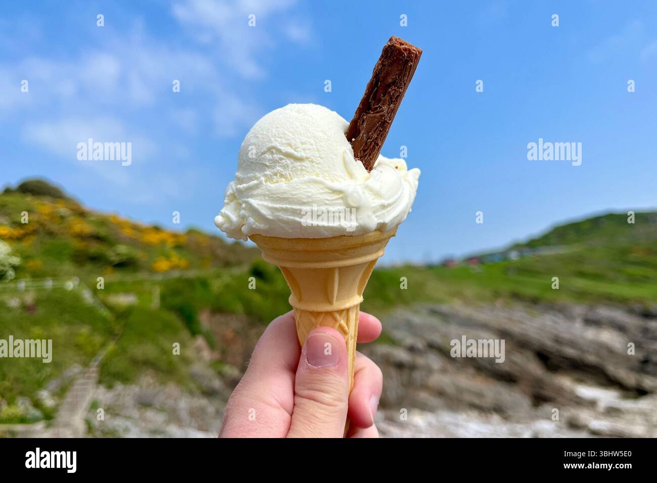 Person's hand holding an Ice Cream Cone with a Flake by the seaside in Mumbles. Swansea, Wales, United Kingdom. 2nd May 2025. - Smartphone Captured Stock Image Person's hand holding an Ice Cream Cone with a Flake by the seaside in Mumbles. Swansea, Wales, United Kingdom. 2nd May 2025. - Smartphone Captured Stock Image