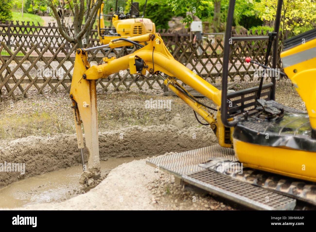 Yellow Digging Machine A yellow excavator is actively digging a trench in a garden area ...