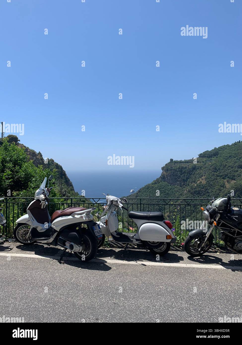 Two scooters outside on a sunny day overlooking green hills and the ocean - Smartphone Captured Stock Image