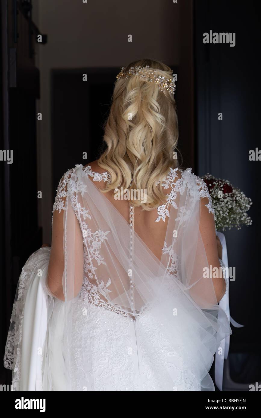 Back view of a bride wearing a delicate lace gown and golden floral ...