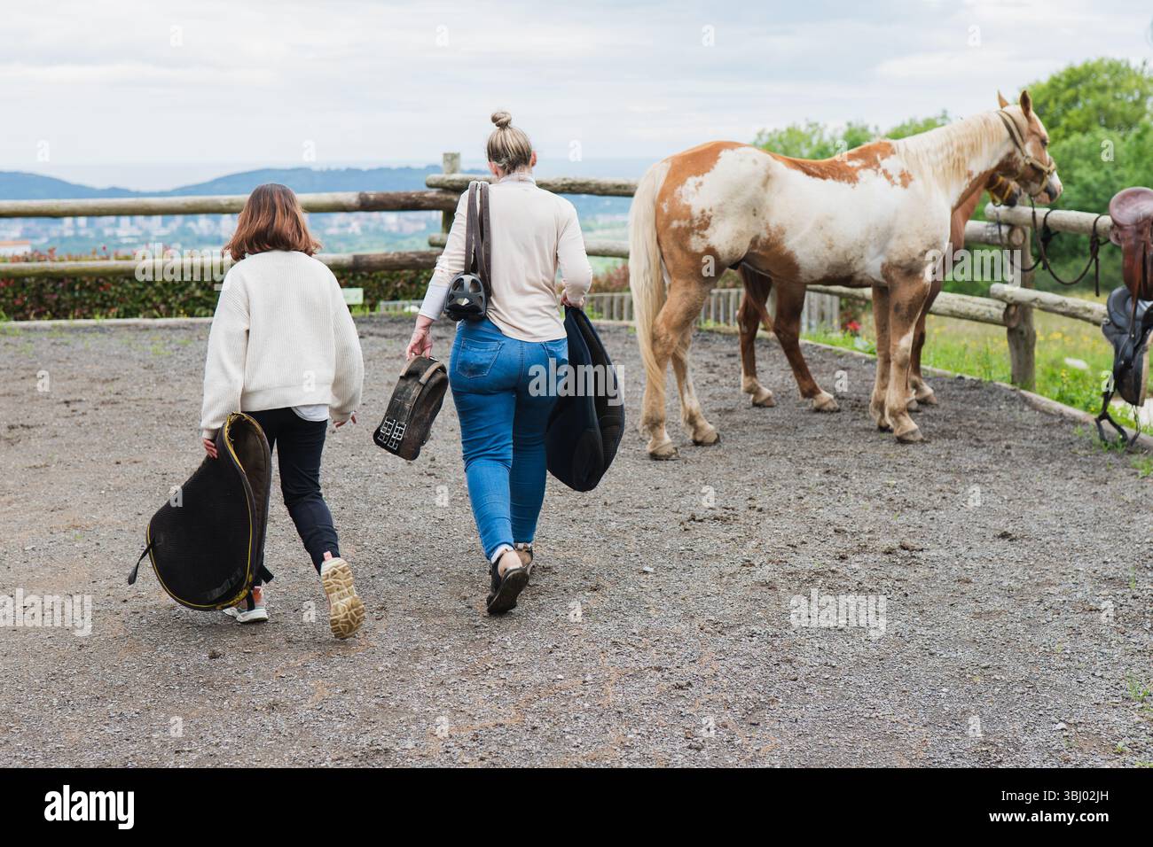 A family spends a delightful day at a farm, walking towards a horse. They carry equipment, ready for a day of riding and bonding amidst the tranquil f Stock Photo