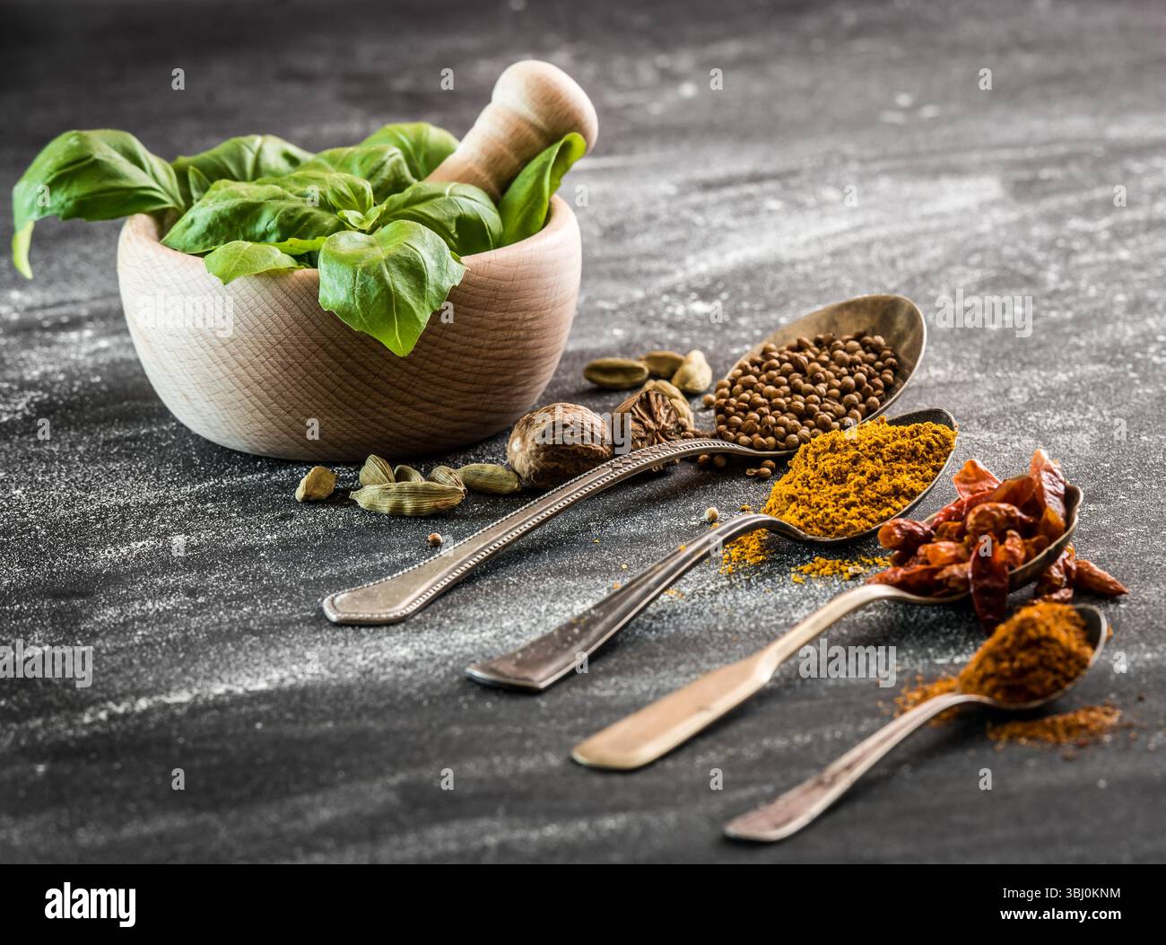 fresh basil in a wooden mortar and spices spoons Stock Photo