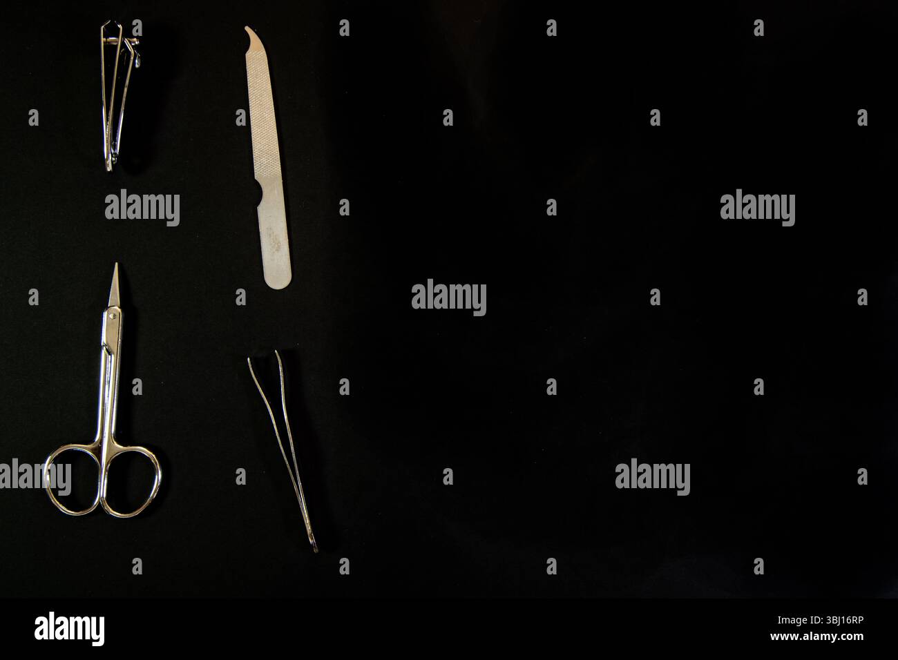 Nail grooming kit with clippers, file, scissors, and tweezers neatly arranged on a black background—clean, minimalist personal care tools. Stock Photo