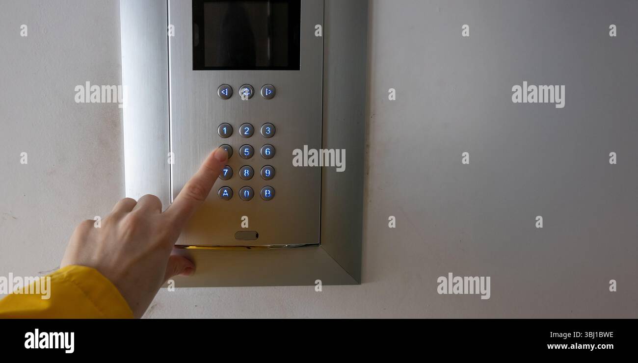 A human hand presses buttons on a keypad at the entrance of an ...