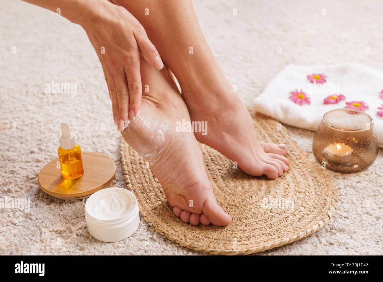 Applying heel cream in a home spa with candle, oil, and towel. Wellness, beauty, and hydration skincare ritual for soft and healthy feet. Stock Photo