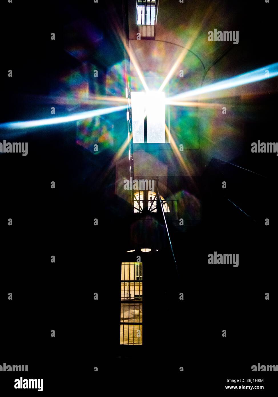 A bright light shines through a window, creating a starburst effect with colorful refractions. The image is taken from a dark interior, possibly a bui Stock Photo