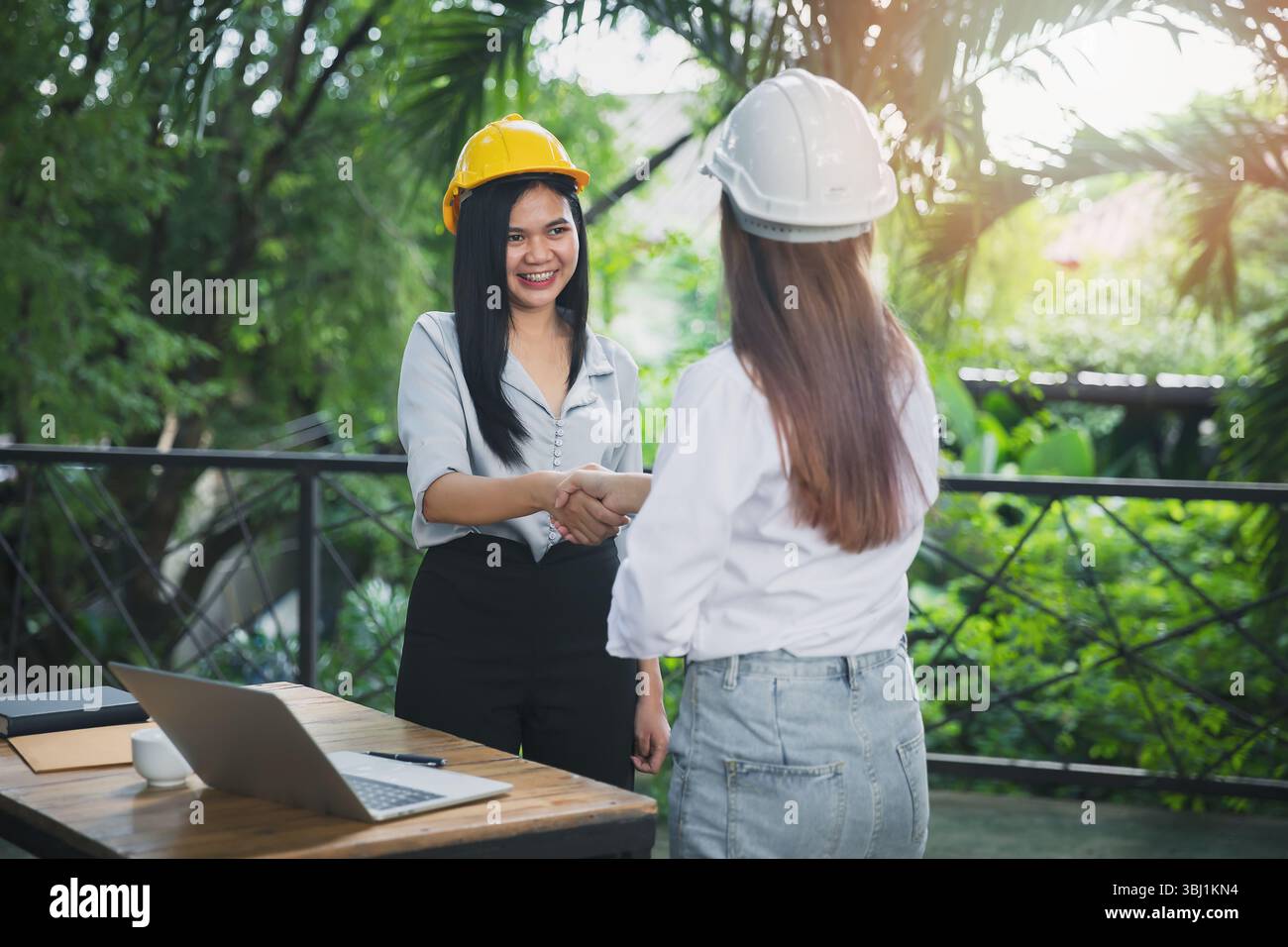 Two asian female architect and engineer in protective helmets shaking hands after meeting. Success collaboration concept. Stock Photo