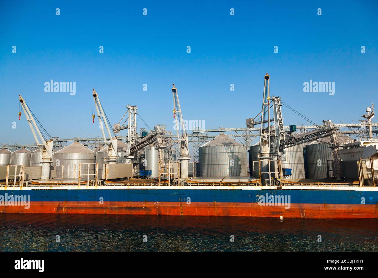 Cargo transport ship is moored at grain storage terminal with storage ...