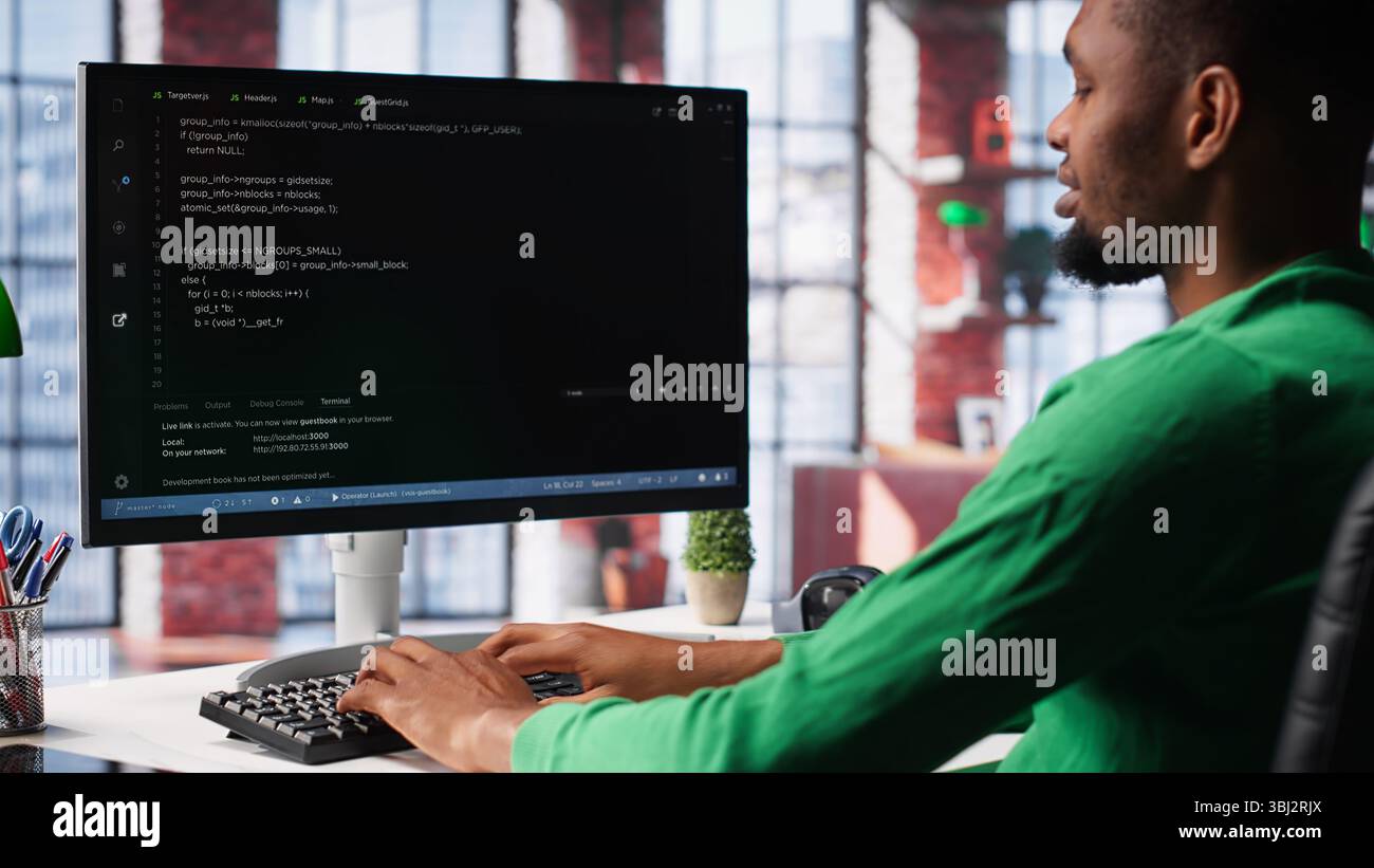 Male programmer types code on computer and running script, programming language. African american IT expert in modern loft fixing errors within the software, implementing new features. Camera A. Stock Photo