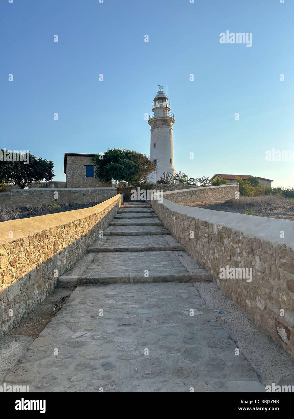 Stone pathway leading to the iconic white lighthouse in Paphos, Cyprus, captured in soft evening light under a clear blue sky. - Smartphone Captured Stock Image