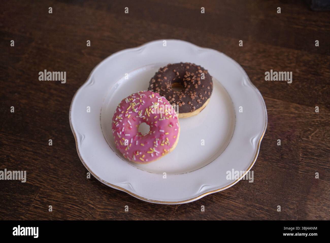 Donuts with chocolate and pink icing on a white plate on a wooden table Stock Photo