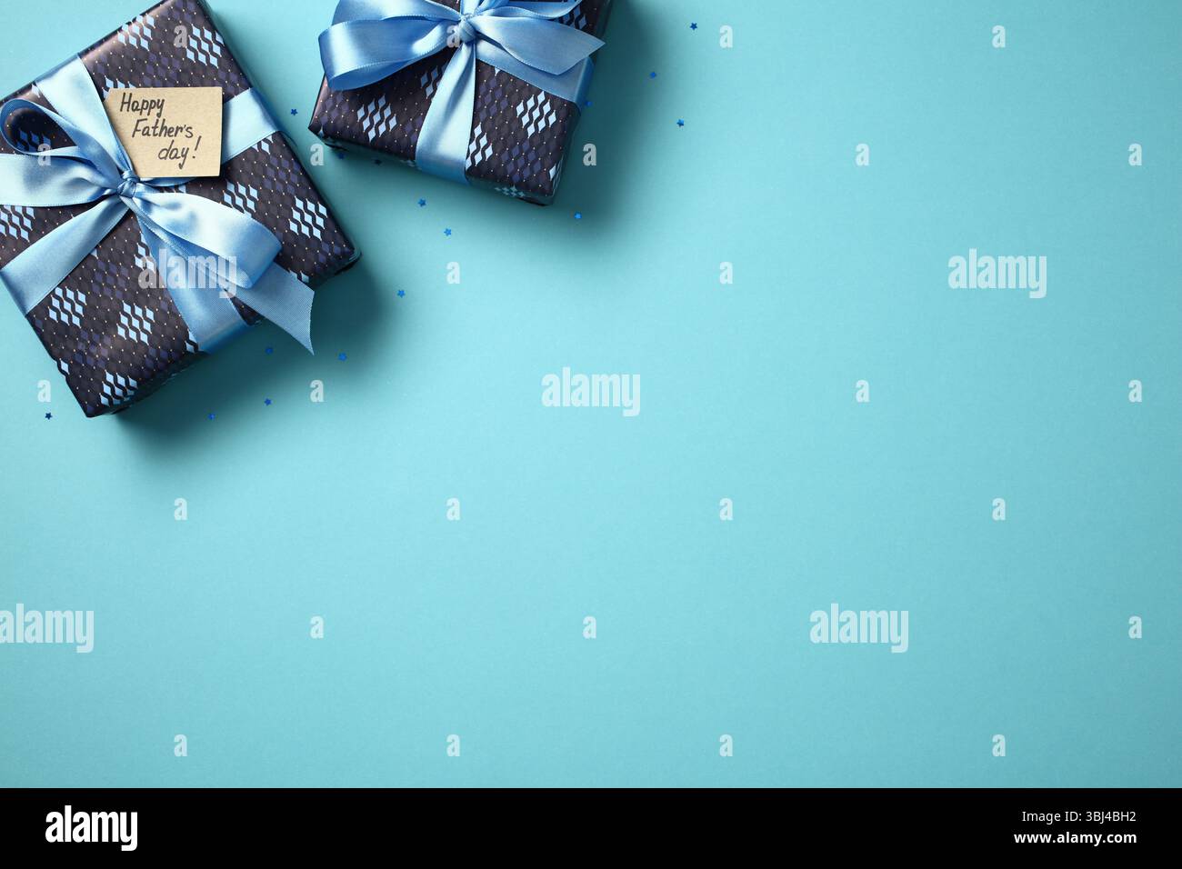 Father's Day gifts flat lay. Two blue gift boxes with ribbons and 'Happy Father's Day' tag on blue background with confetti. Top view, copy space. Stock Photo