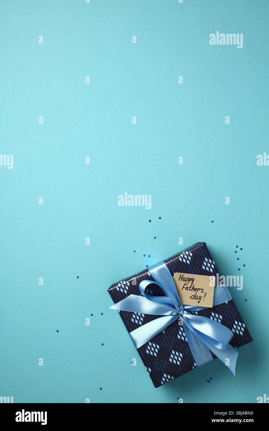 Father's Day gift box with blue ribbon and "Happy Father's day!" tag on a light blue background. Top view, flat lay concept for holiday celebration. Stock Photo
