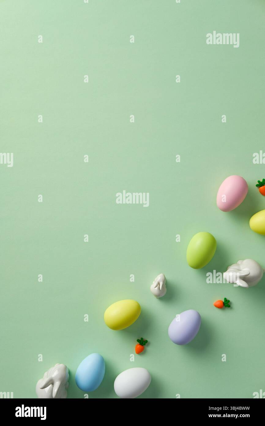 Easter flat lay composition. Top view pastel colored Easter eggs with ceramic bunnies on green background Stock Photo