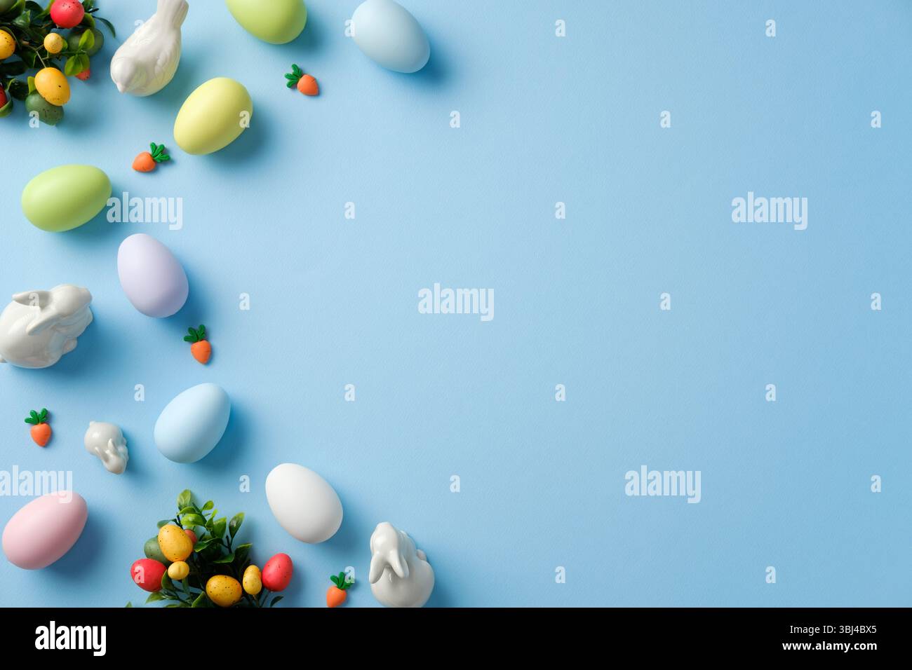 Easter flat lay composition with pastel colored Easter eggs, bunnies, decorations on blue background. Top view with copy space. Stock Photo
