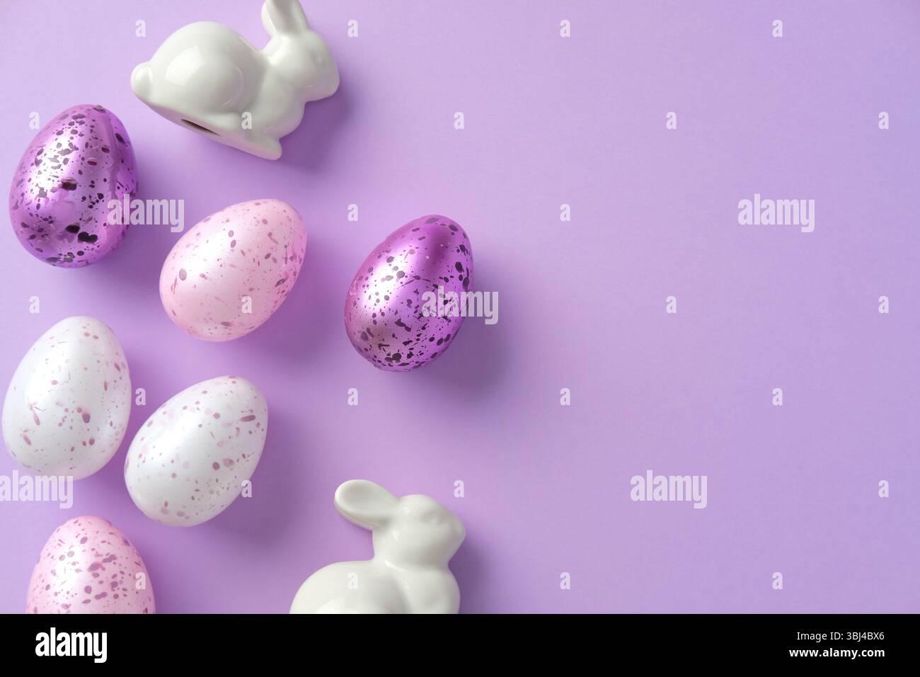 Happy Easter concept. Flat lay composition with purple and white painted Easter eggs, ceramic bunnies on pastel purple background Stock Photo