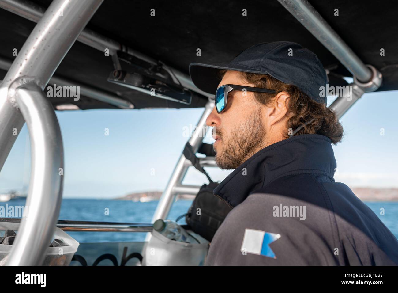 Boat captain wearing sunglasses and a cap concentrating on driving a ...