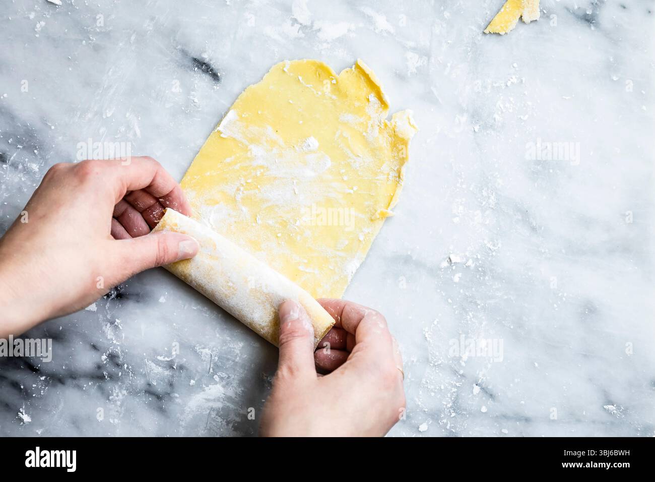 Hands rolling out dough on a floured marble surface. Stock Photo