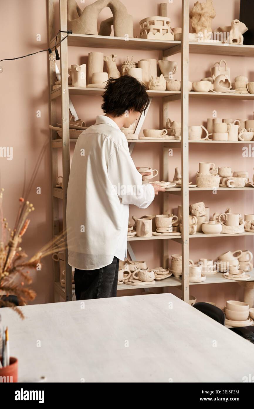 A trendy man examines unique pottery pieces in a vibrant studio full of artistic inspiration. Stock Photo