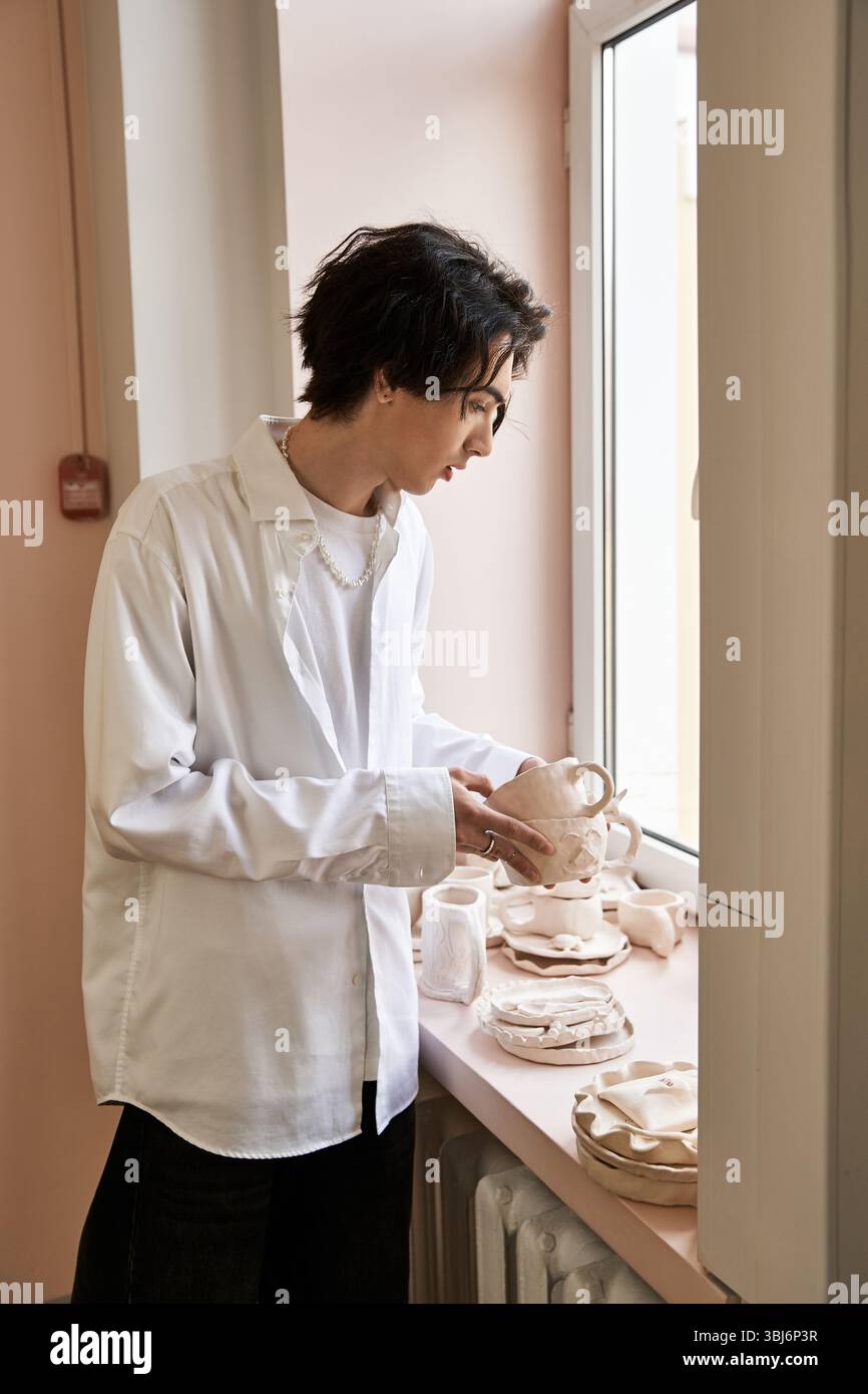 A talented man examines his ceramic creations in a bright pottery studio filled with inspiration. Stock Photo