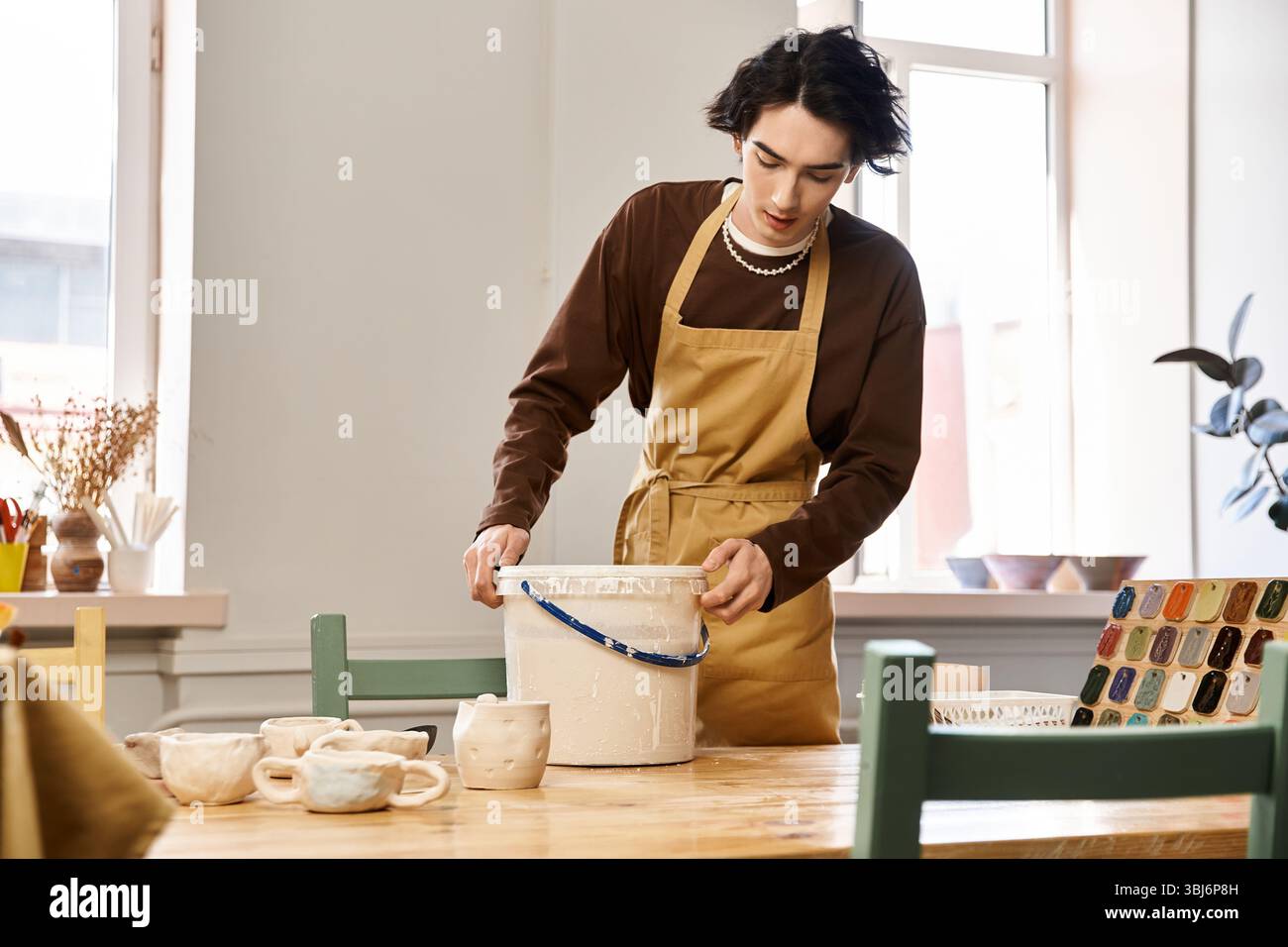 A skilled man passionately works on pottery while surrounded by artistic materials and tools. Stock Photo