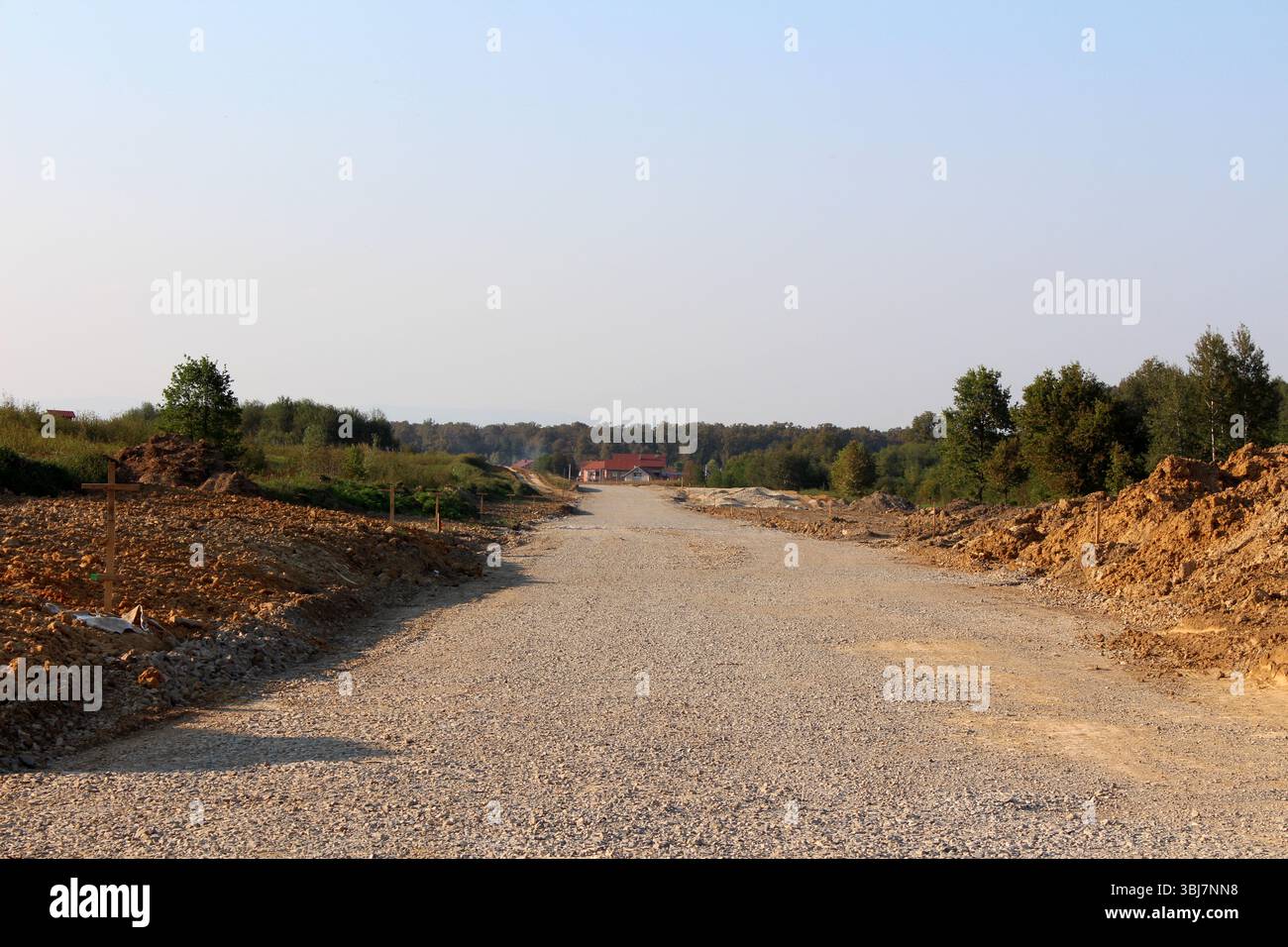Wide gravel road under construction stretches towards a distant house ...