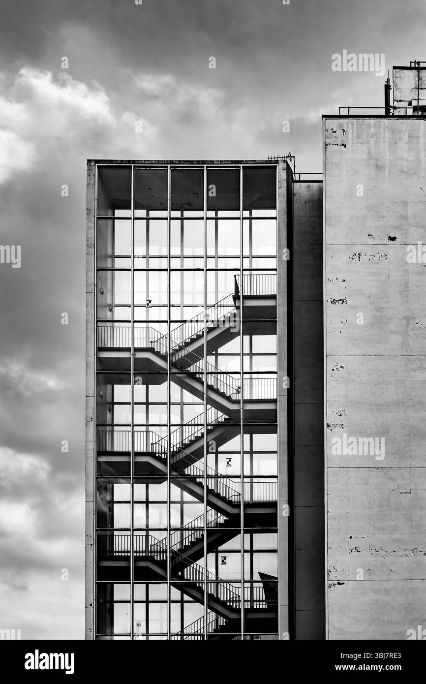 Black and white image of a modern 1960s building with an external glass geometric staircase against a cloudy sky manchester university  uk Stock Photo