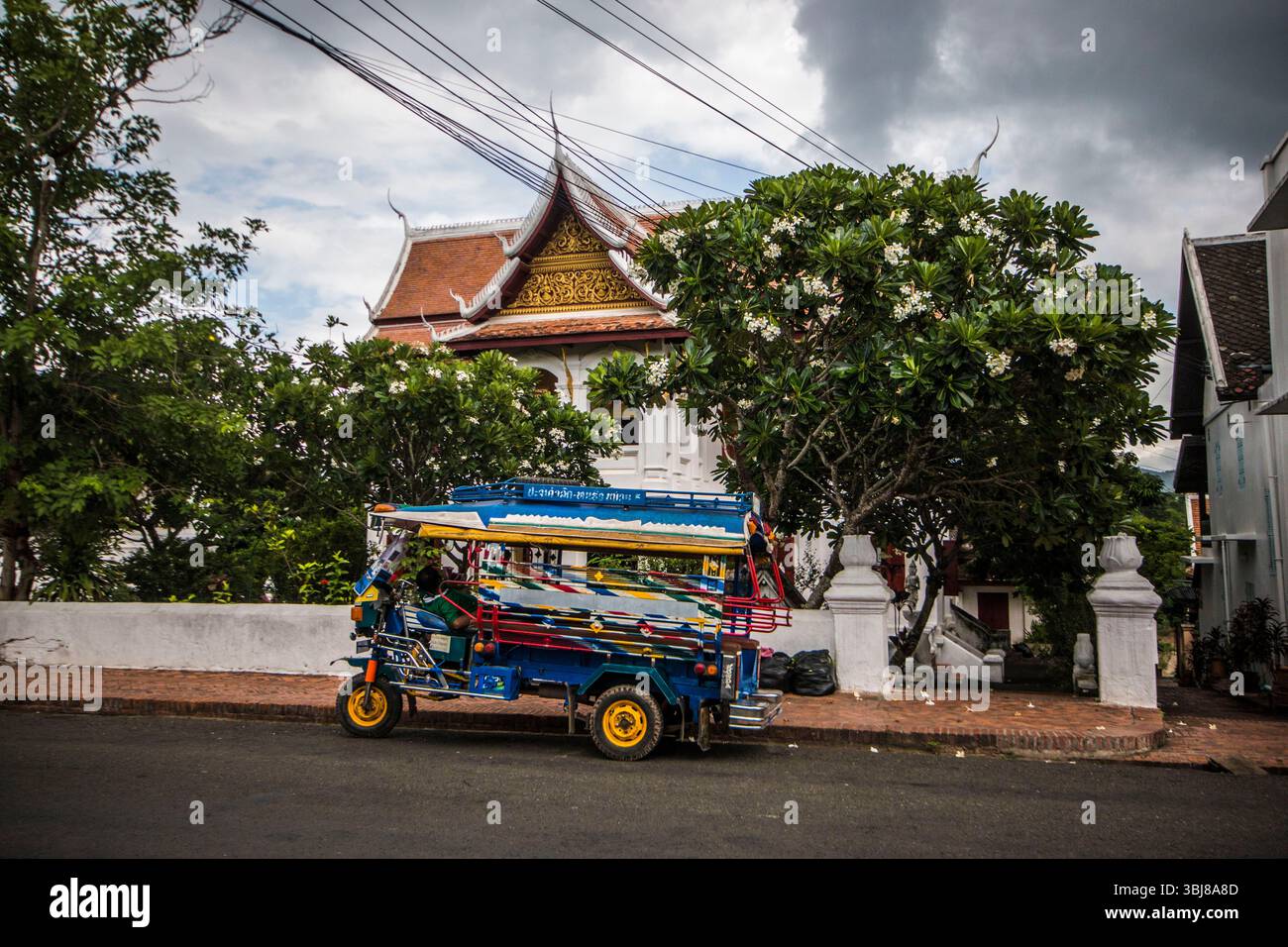 Tuk tuk or rickshaw in front of a french colonial era temple in Luang ...