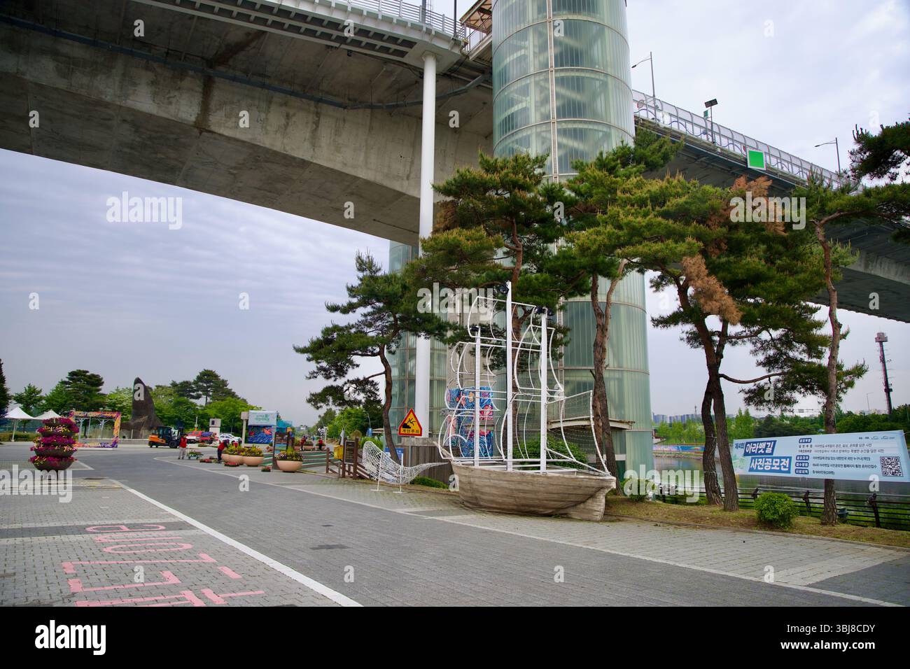 Incheon, South Korea - May 19th 2025: A wire-frame sailboat sculpture and pine trees frame the base of Gyeyang Bridge’s elevator, part of a landscaped Stock Photo