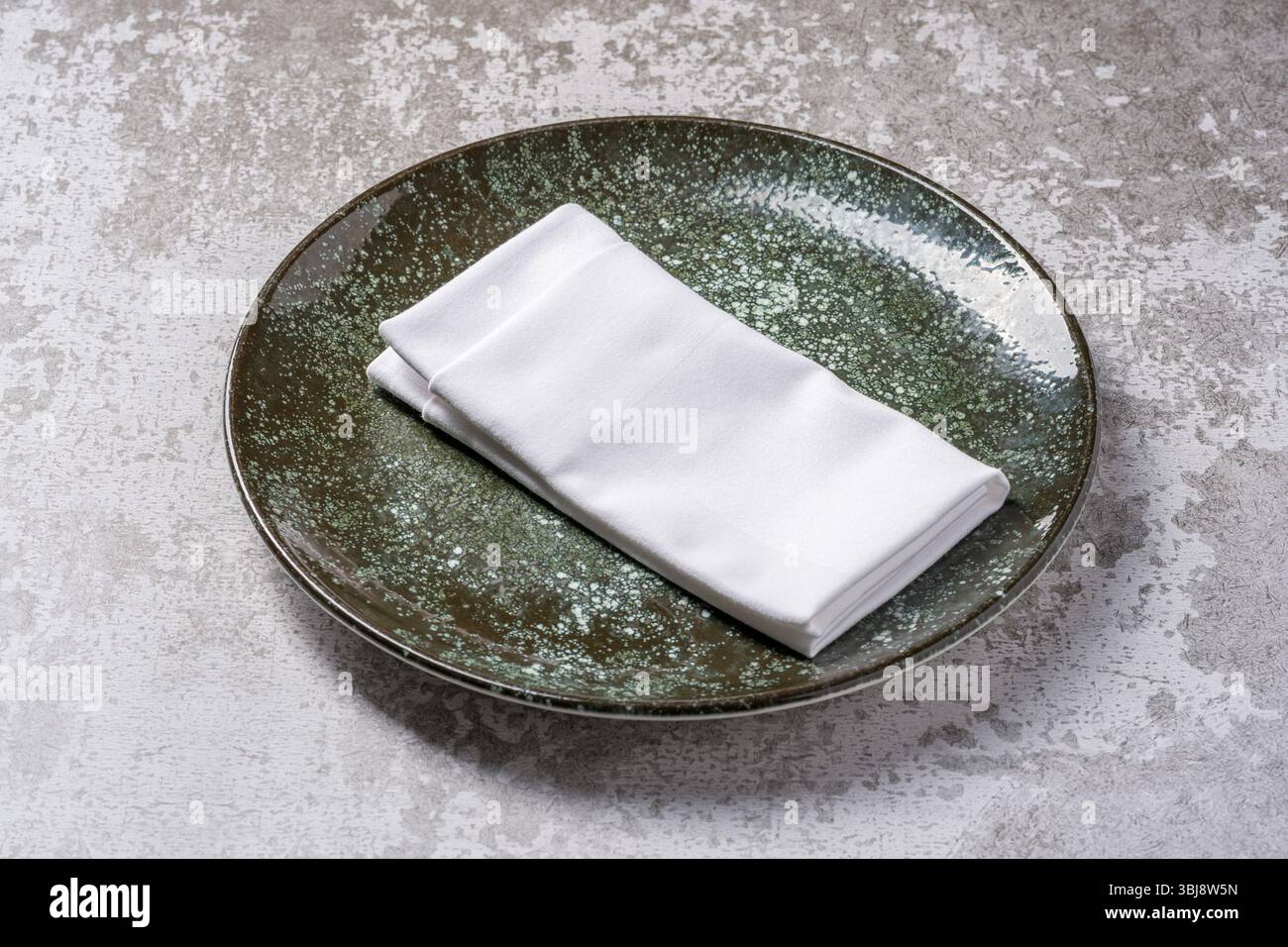 Elegant green ceramic plate with folded white napkin on stone Stock Photo