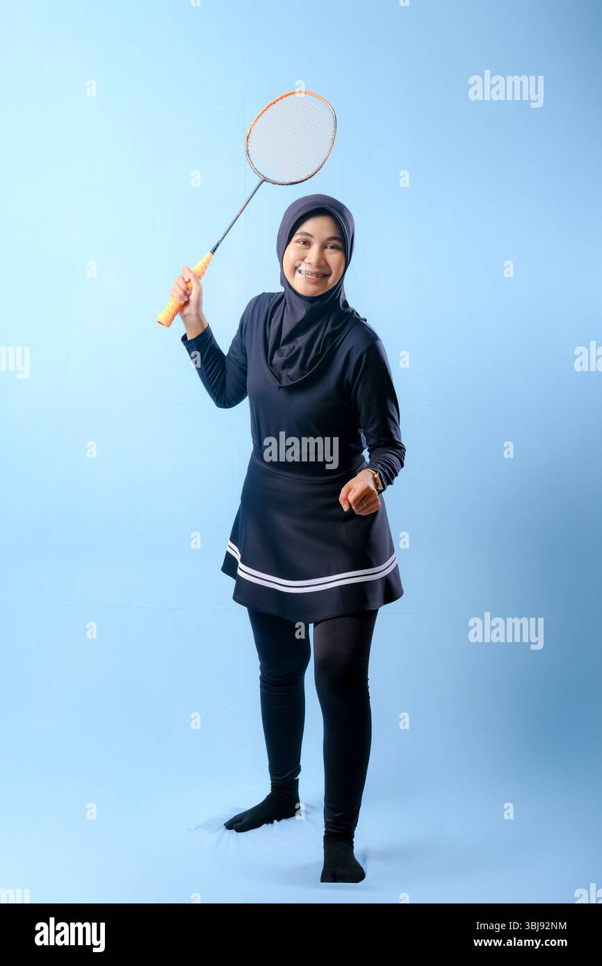 A woman in a black skirt and black pants holding a badminton racket. She is smiling and she is happy Stock Photo