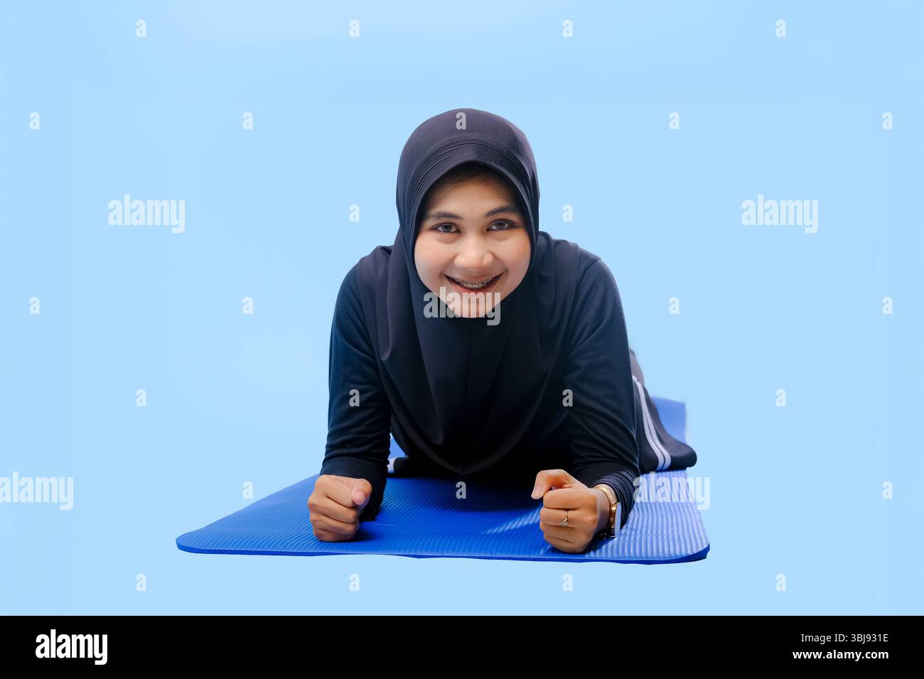 A woman in a black hijab is lying on a blue mat. She is smiling, and she is enjoying herself Stock Photo