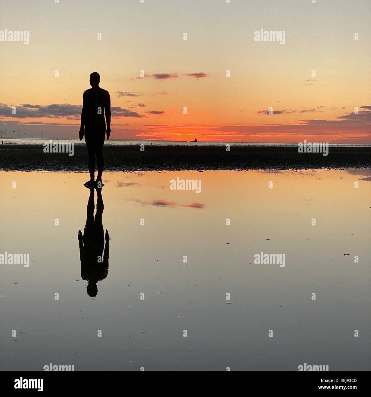 One of Anthony Gormley's Another Place Iron Man statues and vivid red sunset sky at Crosby beach reflected in a calm clear tide pool - Smartphone Captured Stock Image