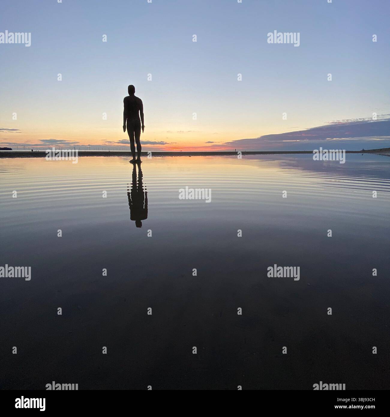 One of Anthony Gormley's Another Place Iron Man statues and vivid red sunset sky at Crosby beach reflected in a calm clear tide pool - Smartphone Captured Stock Image
