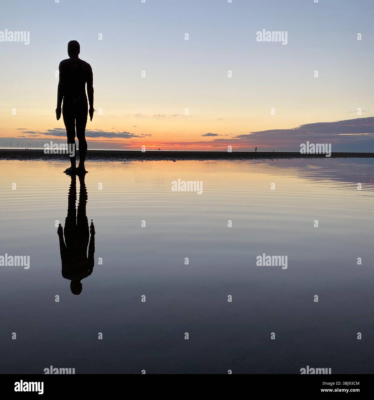One of Anthony Gormley's Another Place Iron Man statues and vivid red sunset sky at Crosby beach reflected in a calm clear tide pool - Smartphone Captured Stock Image