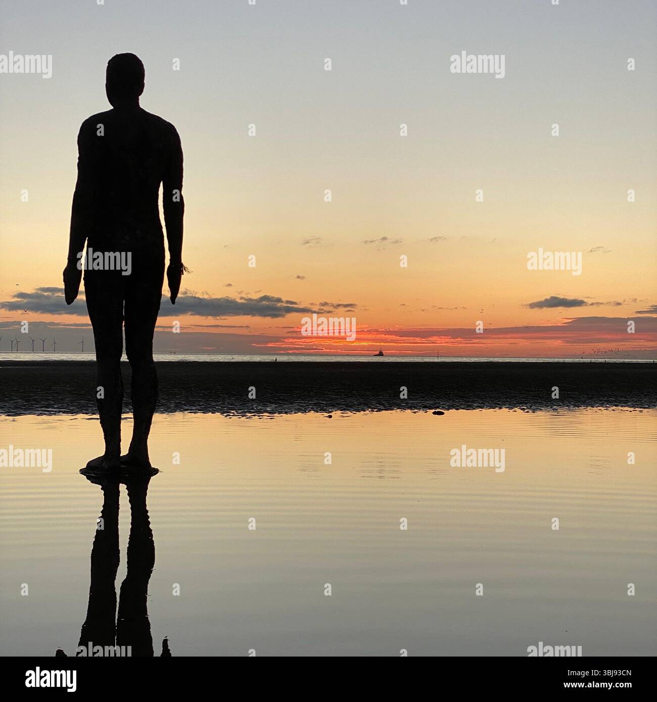 One of Anthony Gormley's Another Place Iron Man statues and vivid red sunset sky at Crosby beach reflected in a calm clear tide pool - Smartphone Captured Stock Image