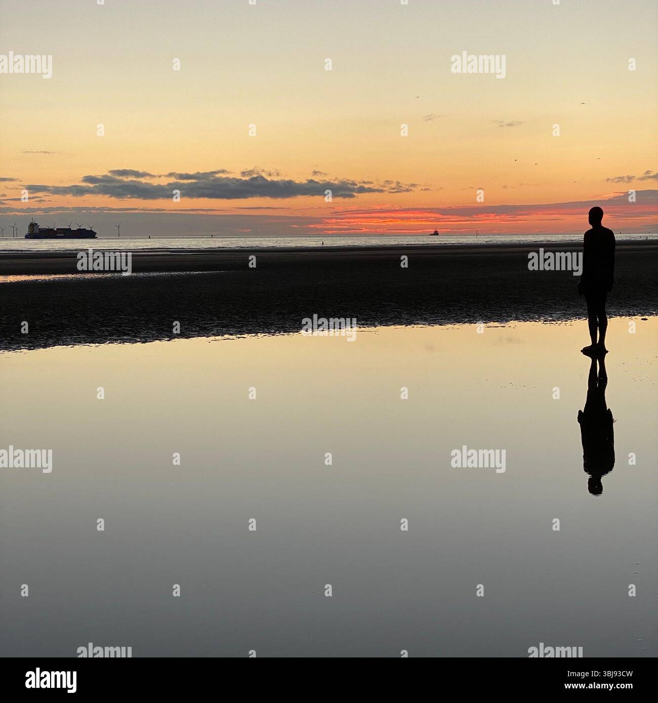One of Anthony Gormley's Another Place Iron Man statues and vivid red sunset sky at Crosby beach reflected in a calm clear tide pool - Smartphone Captured Stock Image