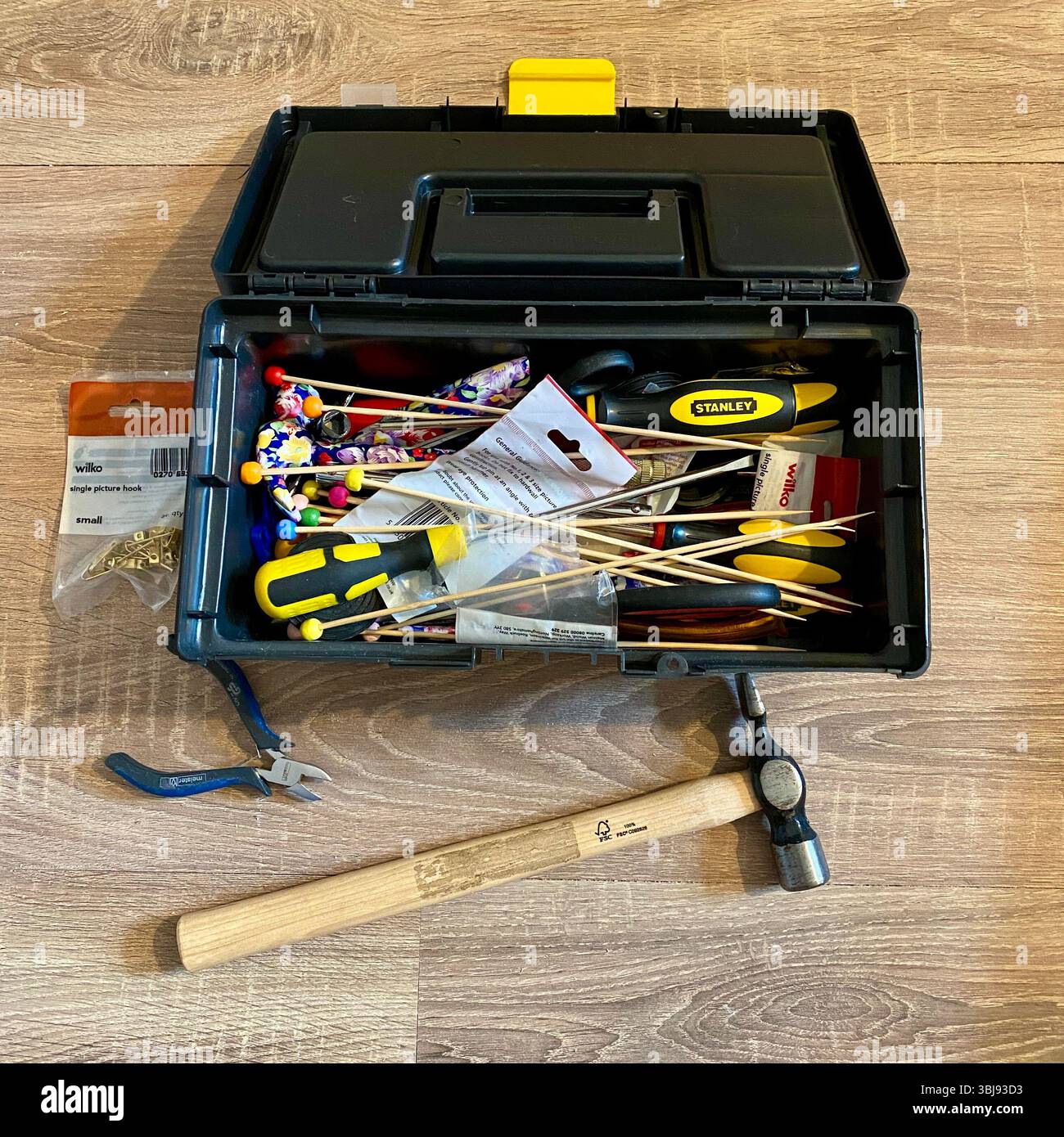 Open black toolbox on floor with various home tools inside and a hammer beside it, ready for DIY or repairs - Smartphone Captured Stock Image
