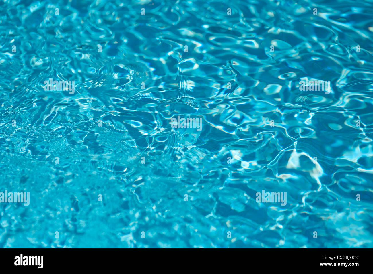 Shallow depth of field details with clear blue and transparent water in a swimming pool during a sunny warm day Stock Photo
