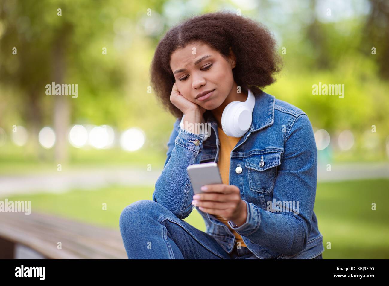 Thoughtful African American female student outdoors looking concerned at smartphone Stock Photo