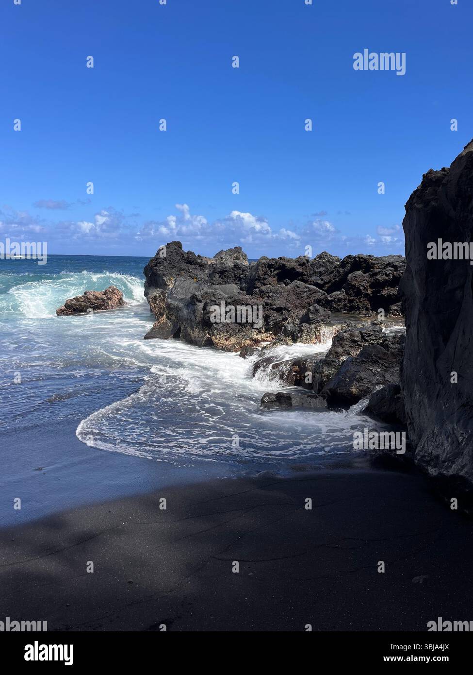 The beautiful and magical black sand beaches on the Big Island of Hawai'i, USA with volcanic black lava rock and crashing waves. - Smartphone Captured Stock Image