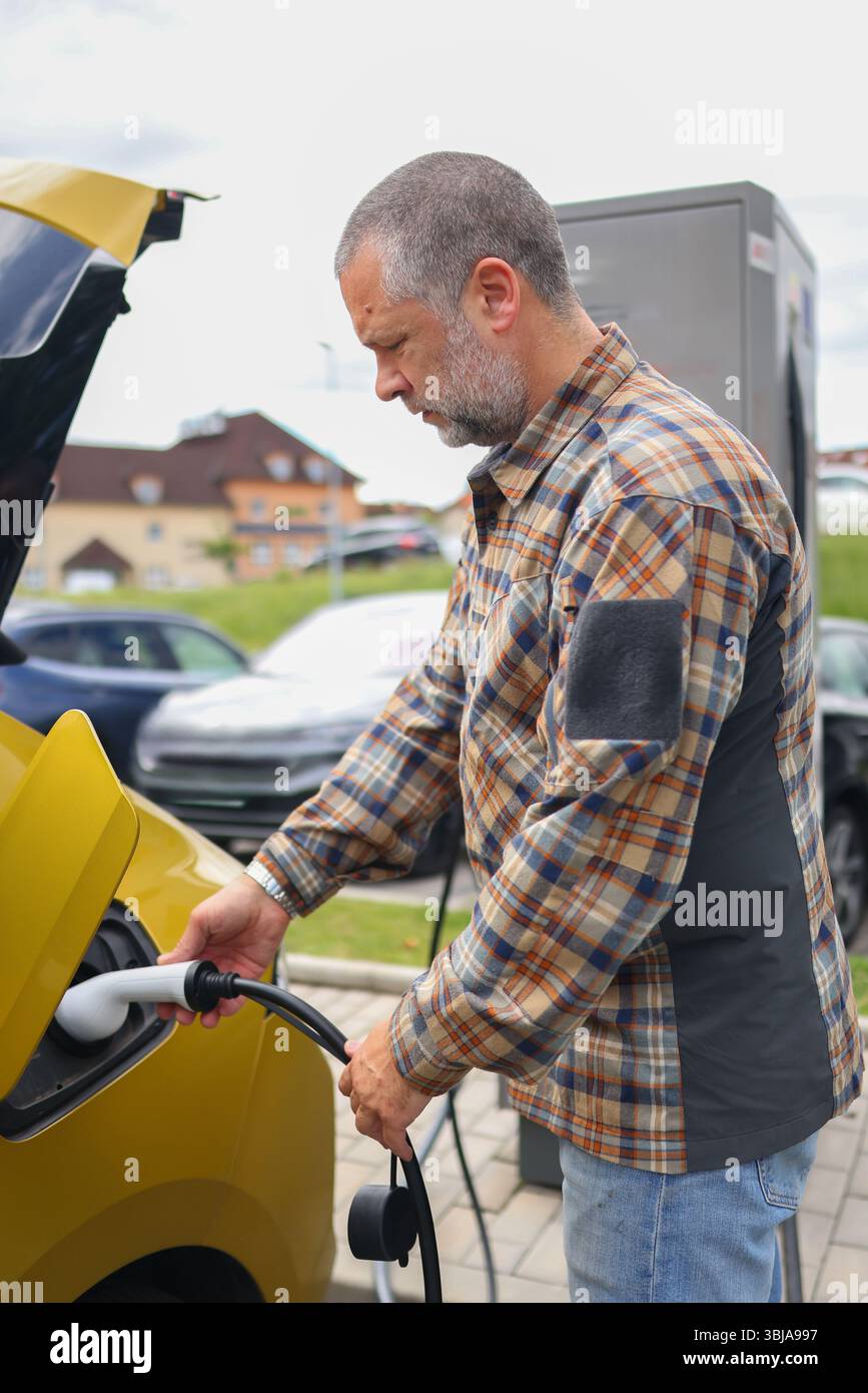 EV charging process with male hand holding connector near electric car socket, eco friendly concept Stock Photo